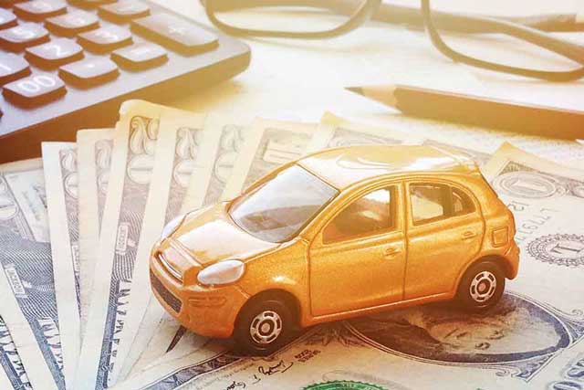 miniature car model on money next to a calculator and pencil